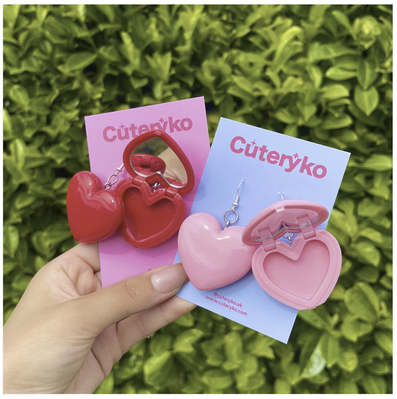 Two sets of plastic love heart shaped earrings which are open to show a hollow and mirror. One pair is red and the other pair is pink. 